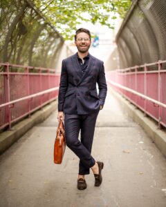 man in black suit jacket and brown pants holding brown leather bag